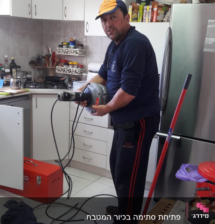 אדם מחזיק מכשיר אינסטלציה במטבח